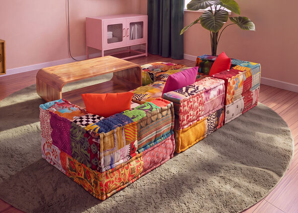 Barvita modularna sedežna garnitura patchwork, postavljena okoli lesene klubske mizice na okrogli preprogi v sodobni dnevni sobi.