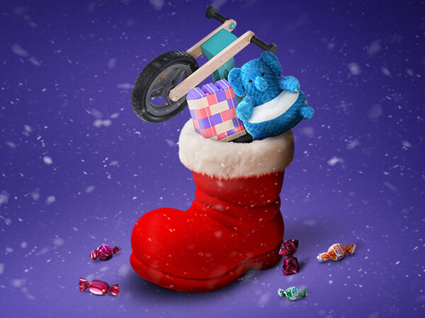 Praznična božična scena z velikim rdečim škornjem z belim kosmatenim robom, polnim daril, na vijoličnem zasneženem ozadju. V škornju so majhno leseno ravnotežno kolo, moder plišasti slon in barvit komplet gradbenih kock za otroke. Okoli škornja so po snegu raztresene barvno zavite bombone. Po zraku padajo snežinke.
