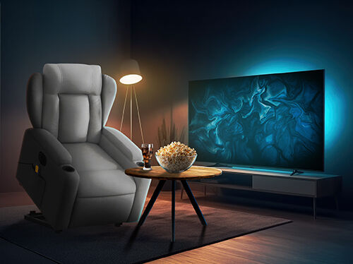 Elegantna dnevna soba z udobnim sivim naslanjačem z nastavljivim naslonom, lesenim mizico s kokicami in pijačo, talno svetilko, ki sveti v kotu, ter velikim ploskim televizorjem z modro ambientalno osvetlitvijo.