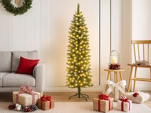 Svetla, moderna praznična scena z visokim, vitkim, vnaprej osvetljenim božičnim drevesom s toplimi belimi lučkami, ki stoji na sredini. Na levi strani se vidi naslonjalo in rokonaslon svetlo sivega kavča z rdečo blazino. Na svetli preprogi v ospredju leži zbirka zavitih daril, povezanih z rdečimi in belimi trakovi ter okrašenih s storži. Na desni strani sta leseni stol in majhna okrogla lesena mizica z laterno in svečo, ki dopolnjujeta prijetno, praznično vzdušje.