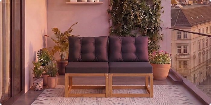  Dvoседežna modularna lesena sedežna garnitura s temno sivimi blazinami na balkonu, obkroženem s sobnimi rastlinami in pogledom na mesto v ozadju